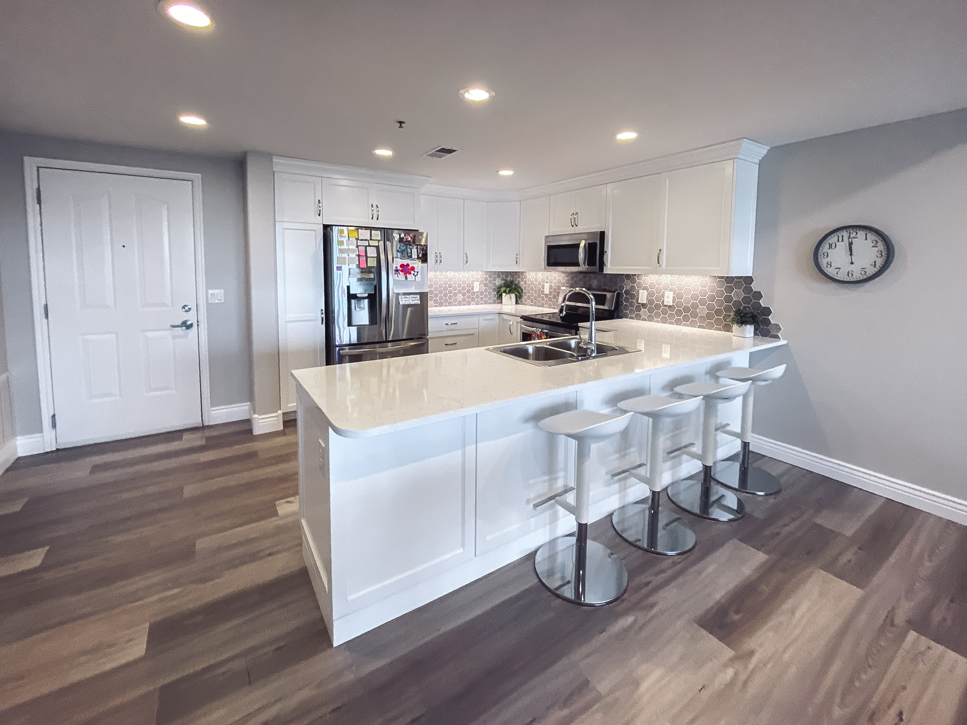 Modern kitchen with white cabinetry, quartz countertops, hexagonal tile backsplash, and a sleek kitchen island with white bar stools.