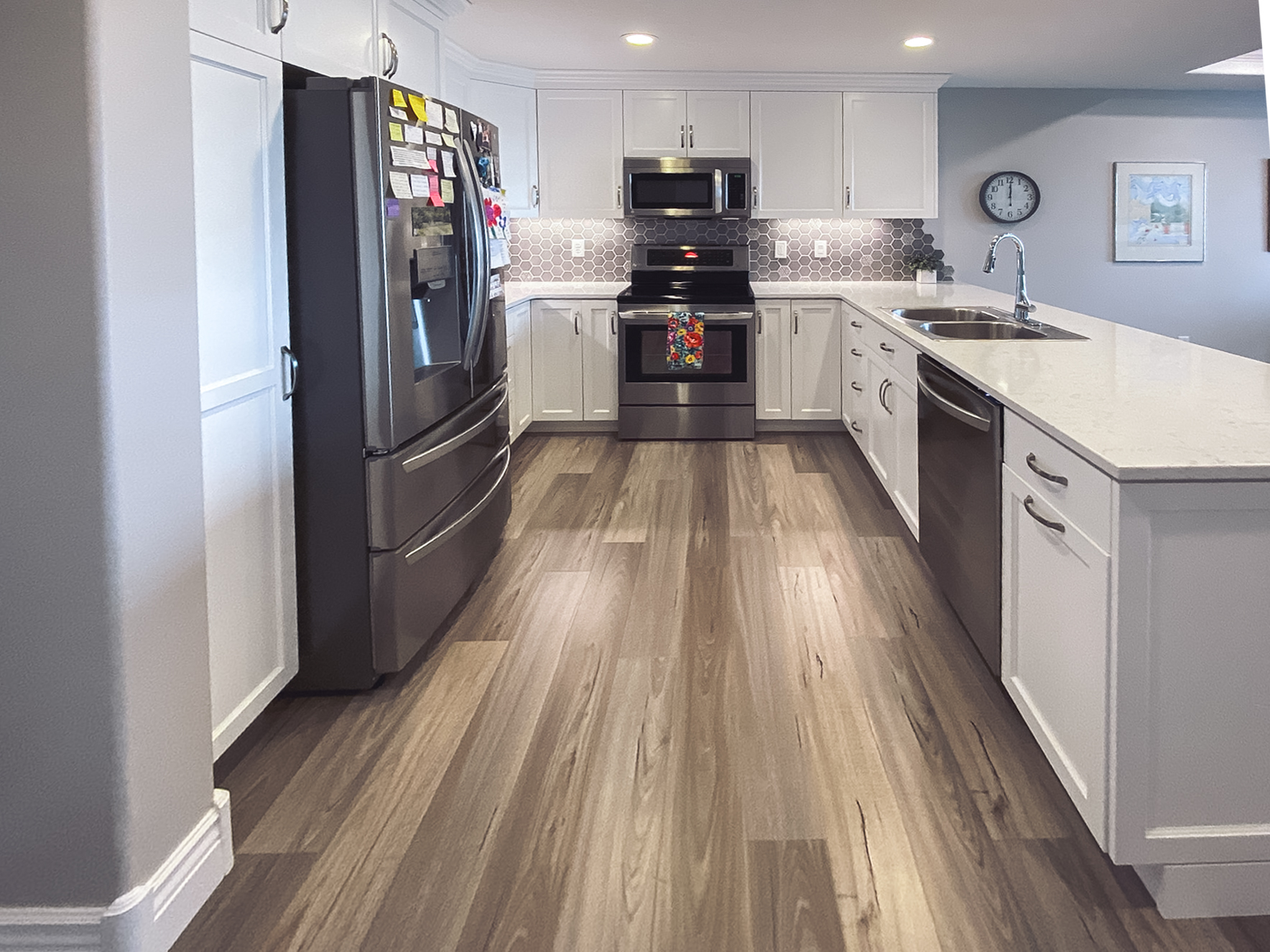 Modern kitchen with white cabinetry, stainless steel appliances, hexagonal tile backsplash, and light wood flooring.