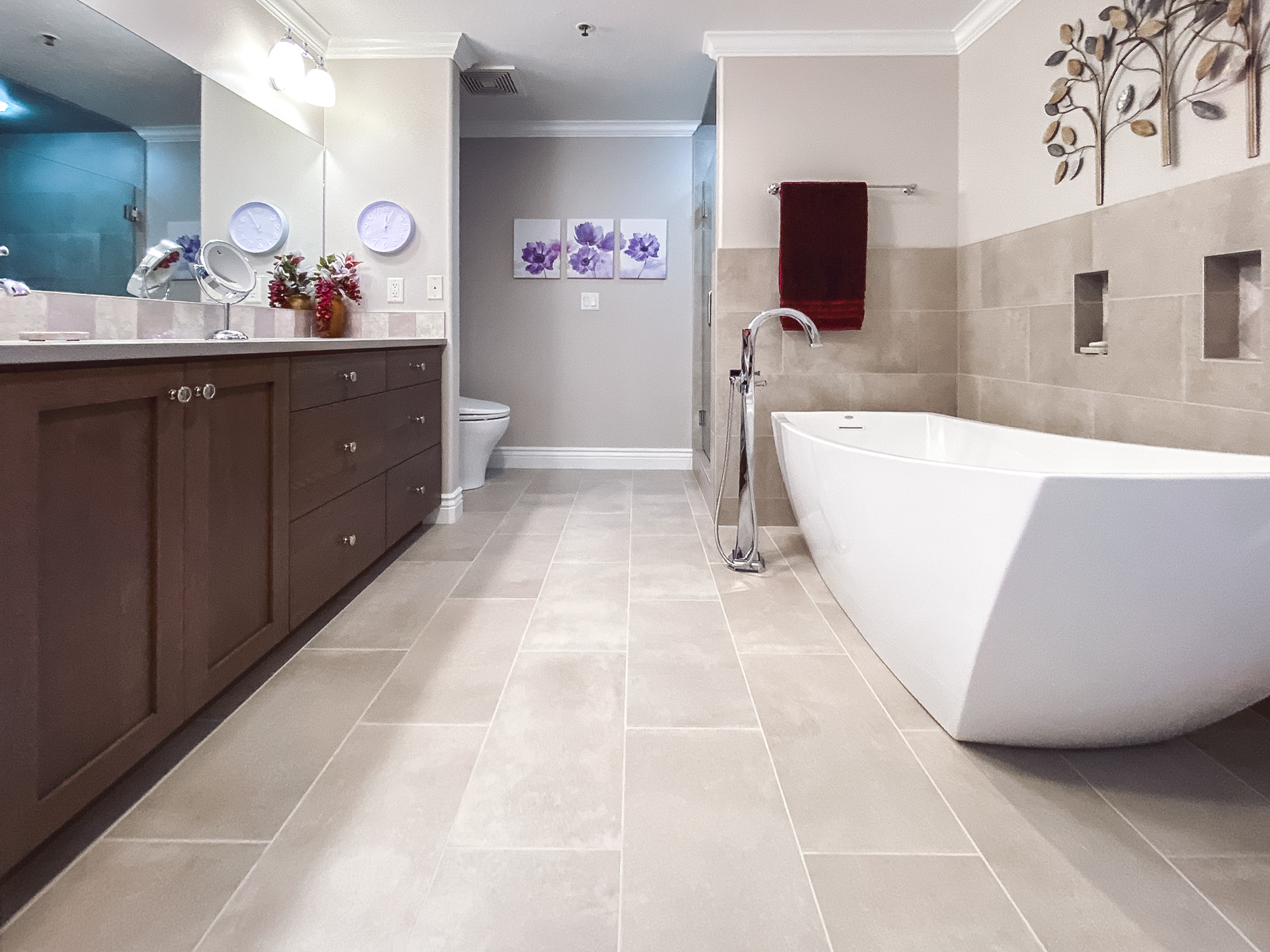 Bathroom with a modern double vanity, freestanding bathtub, and stylish artwork, featuring beige tile floors and a glass-enclosed shower.