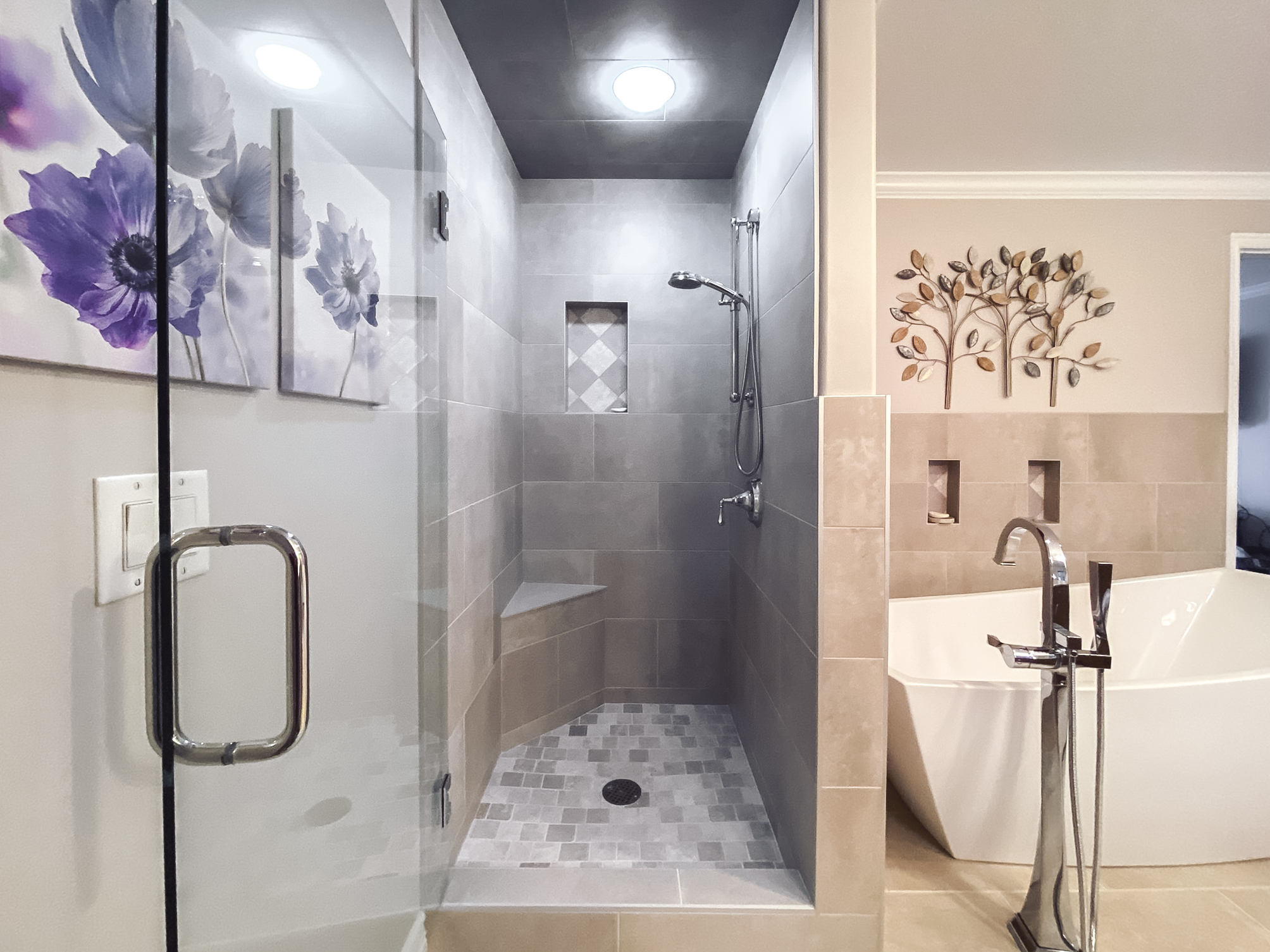Modern bathroom with a glass-enclosed shower featuring gray tile, floral artwork, and a freestanding bathtub.