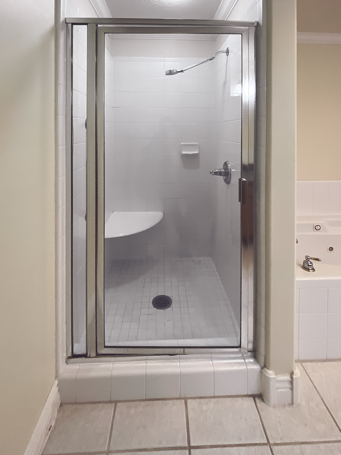 Shower with tiled walls, glass enclosure, and a built-in bench, next to a bathtub with white tiled surround.