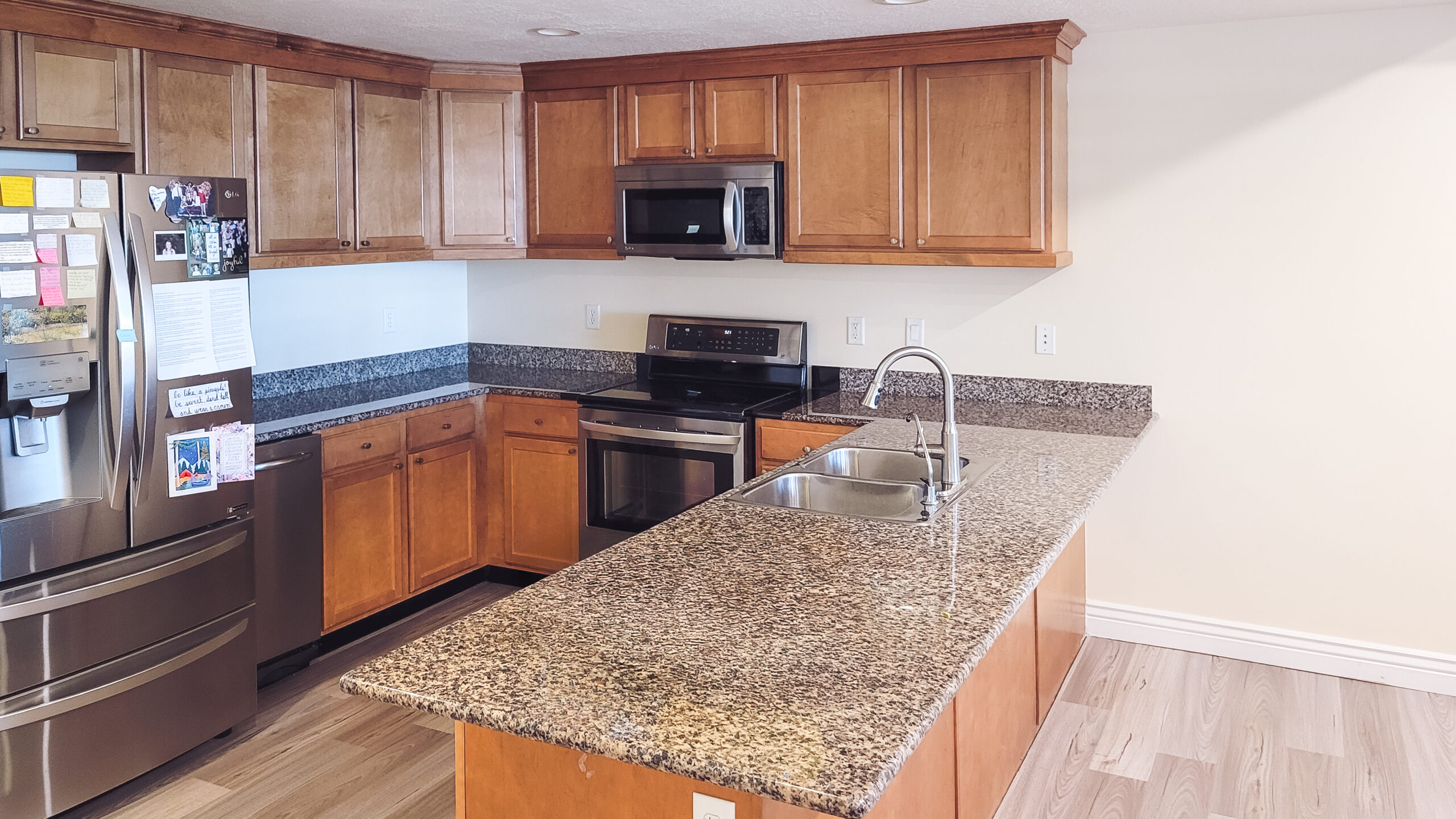 Kitchen with wood cabinetry, stainless steel appliances, granite countertops, and a double sink.