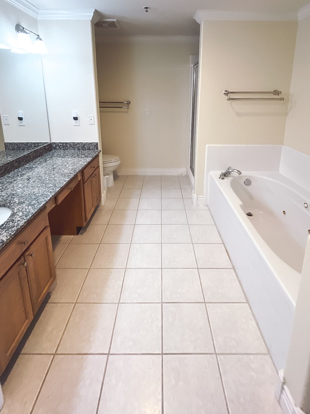 Outdated bathroom with wood cabinetry, granite countertops, white tile flooring, a drop-in bathtub, and separate shower.