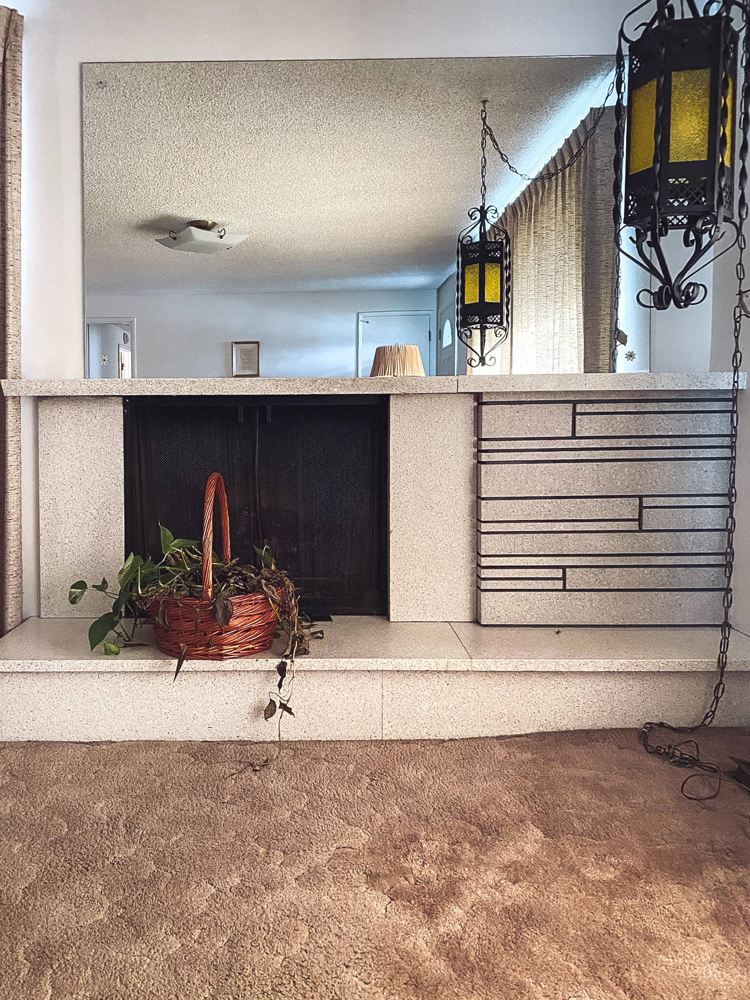 Outdated living room fireplace with stone surround, metal screen, mirror wall, and vintage hanging lanterns.