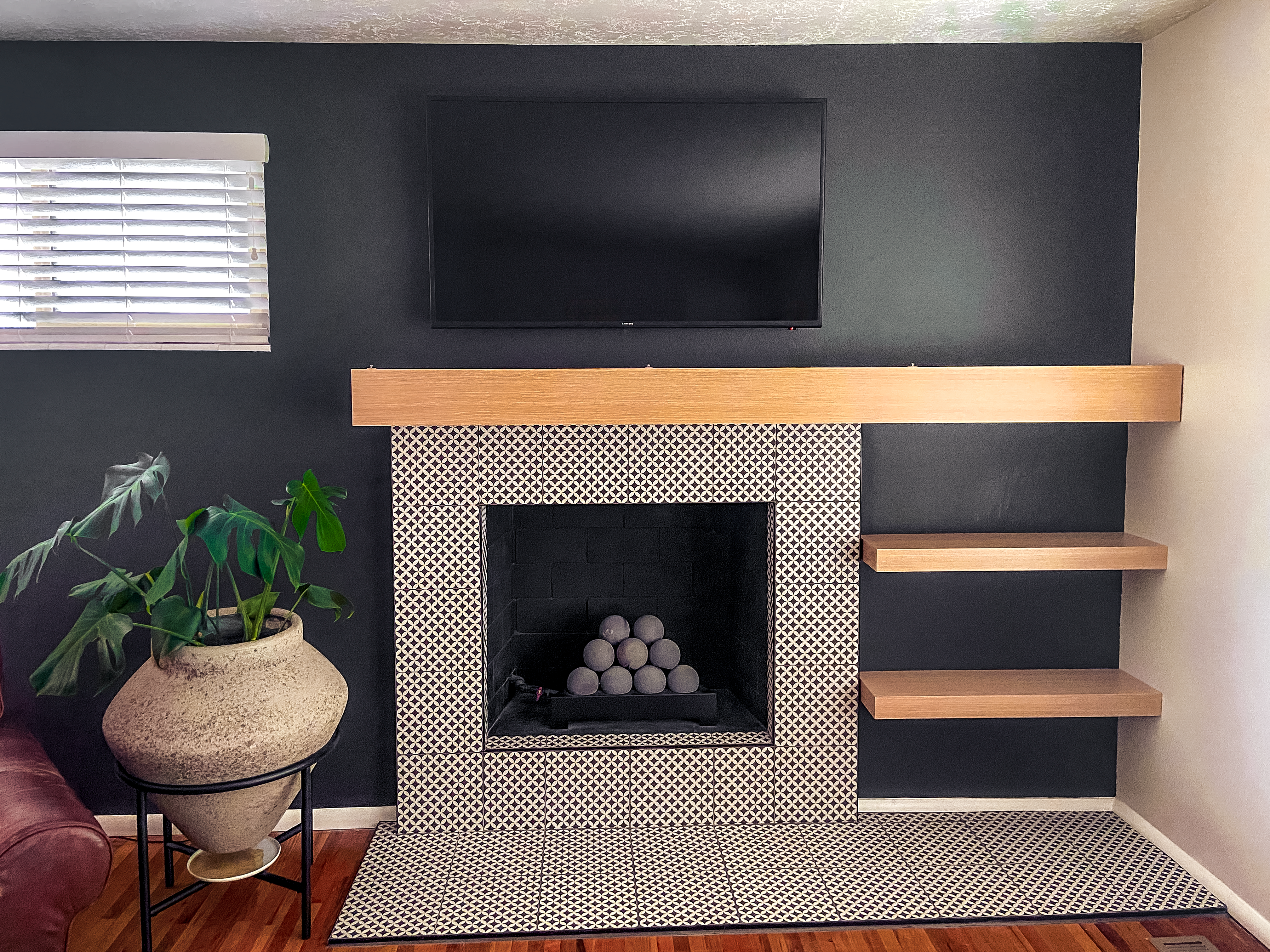 Modern fireplace with wood mantle, built-in shelves, and black accent wall in a completed remodel.
