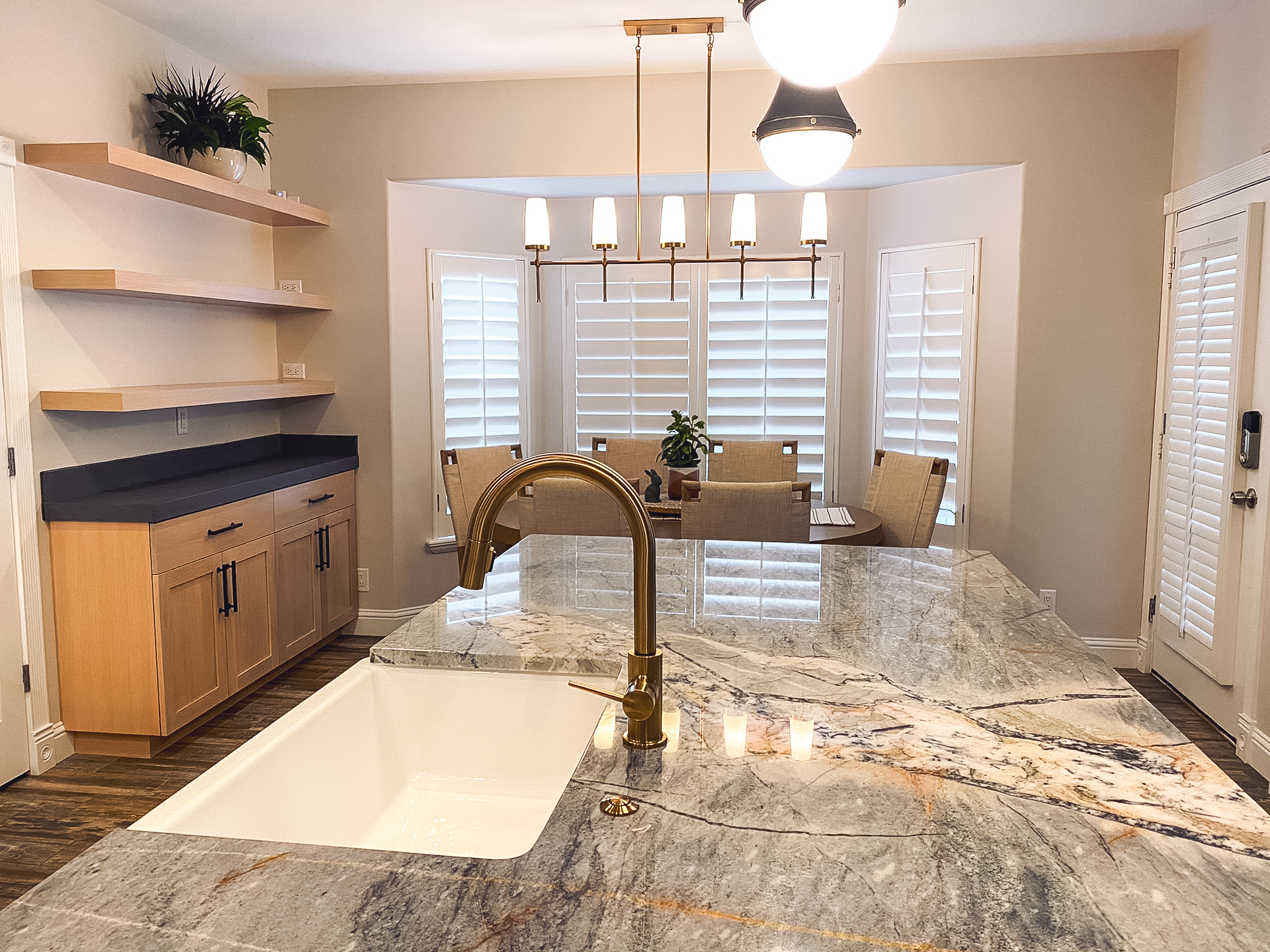 Modern kitchen island with new sink and faucet, floating shelves, dining table, and pendant lighting.